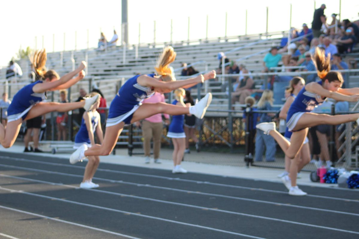 On Sept. 19, 8th grade cheerleaders, Abigail McGuire, Reese Elliot, and Addison Osterman warm up before the football game by practicing their hurdles on the track.