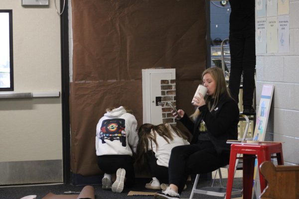 On December 6, Mrs. Armstrong sips her coffee and looks at her phone while, Reese Elliot and Jessie Heitman decorate her door for christmas. Mrs. Armstrong says several students throughout the day have been helping. “7th graders made a snowflakes that are on the house and hanging. 1st hour as they would finish their work they would make candies and frosting” (Armstrong). 