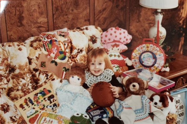 Mrs. Baranski sits in a pile of her toys, a childhood memory from her Christmas  “I think I’m about two years old in this, so this would be 1982. I’m surrounded by all my toys in the world’s itchiest dress!”
