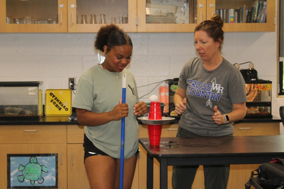 Seventh grader Maci Cavitte demonstrates Newton's third law by hitting a plate with the end of a broom to show that the egg falls into the bottom cup in 3rd hour science on April 26th.
